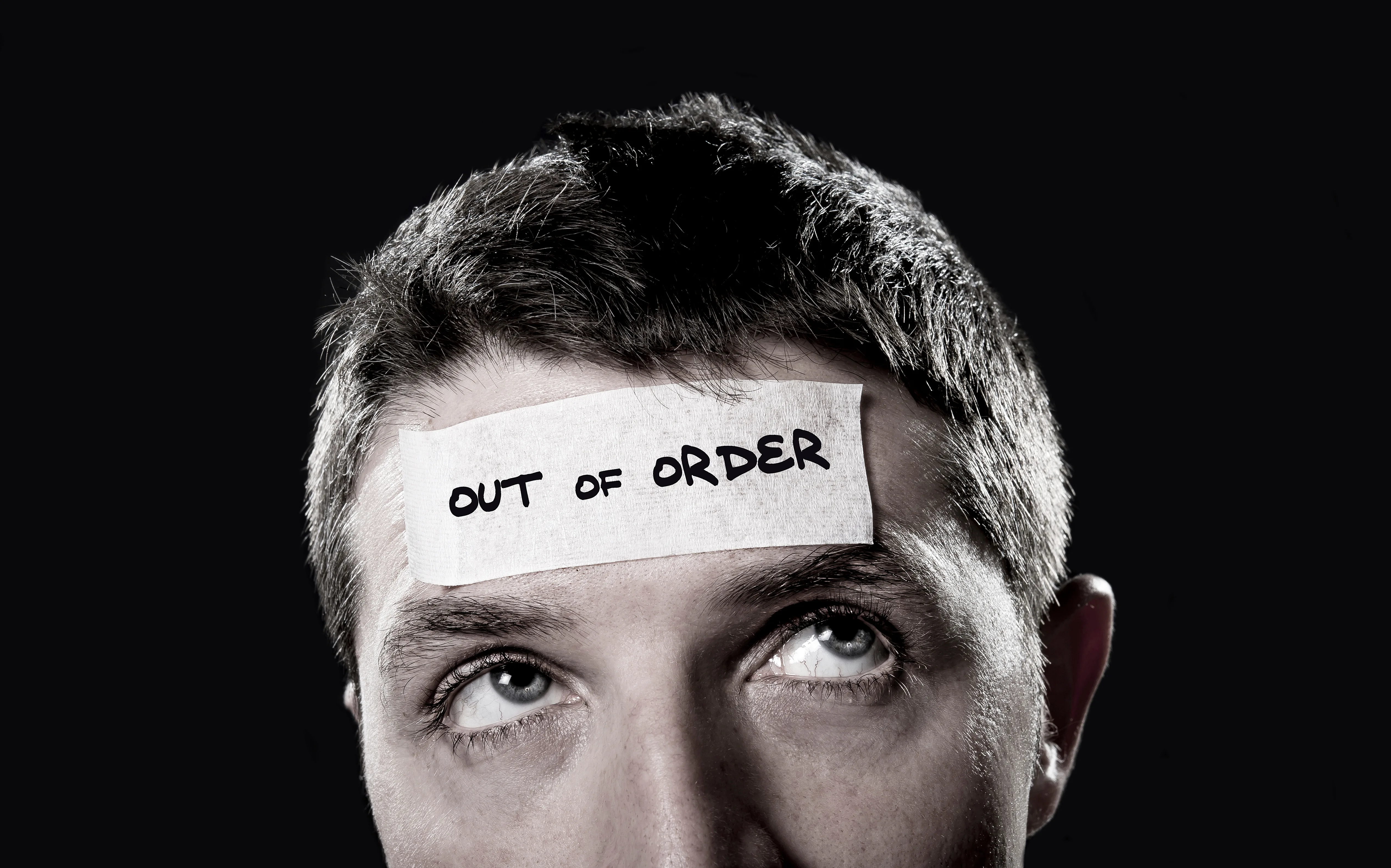 young man with blue eyes and tape text out of order on forehead in empty mind and blank brain concept,  lack of ideas, creativity and mentally tired, overwhelmed and stressed
